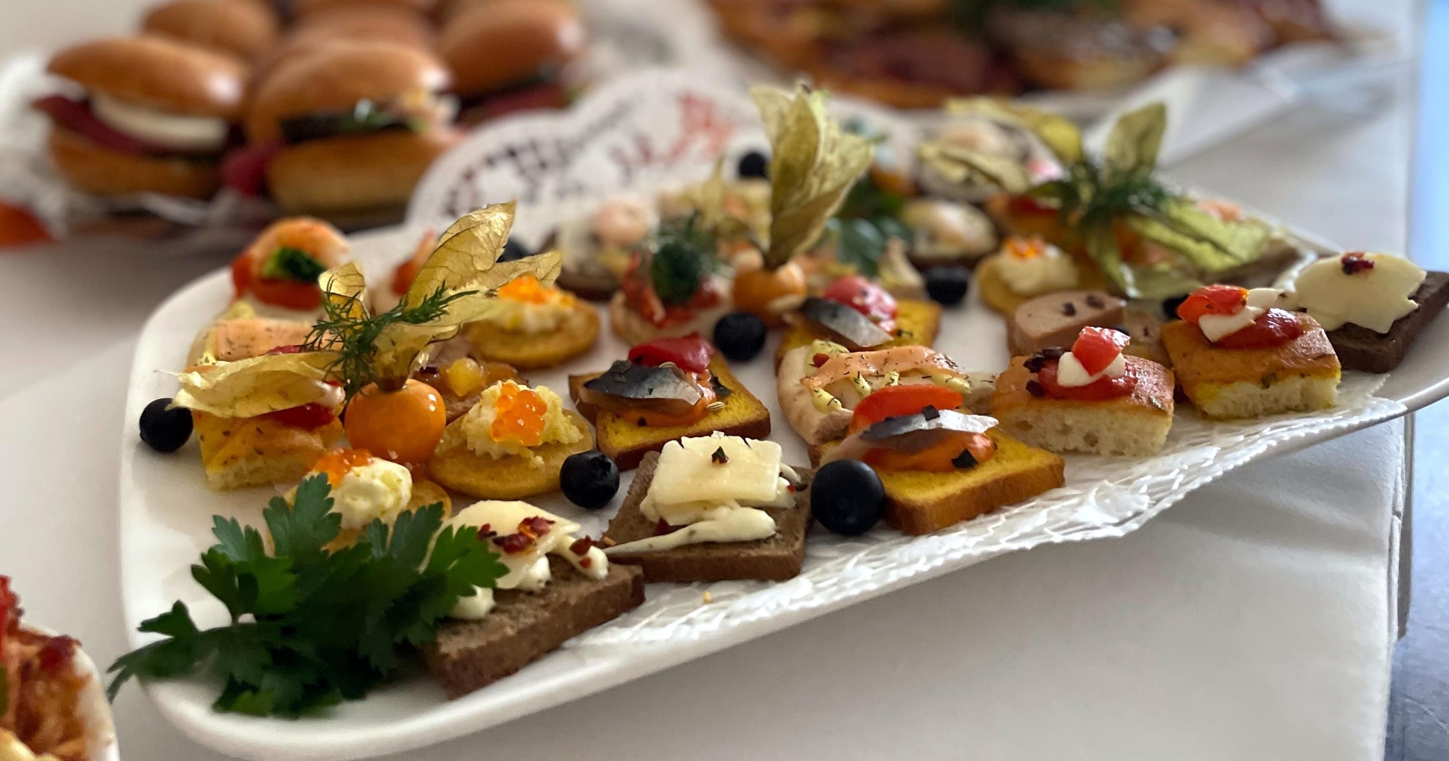 A variety of appetizers on a white platter, including items with cheese, olives, and vegetables.
