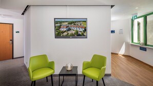 A hotel lobby with two green chairs, a small table with a decorative item, a framed picture on the wall, and a door with a number sign. - Best Western Spreewald (Lübbenau/Spreewald)