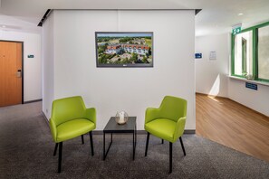A hotel lobby with two green chairs, a small table with a decorative item, a framed picture on the wall, and a door with a number sign. - Best Western Spreewald (Lübbenau/Spreewald)
