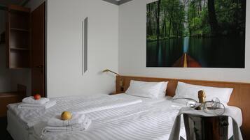 A hotel room with a large bed, a nightstand, a wooden wardrobe, a painting of a forest, and a bottle of champagne.