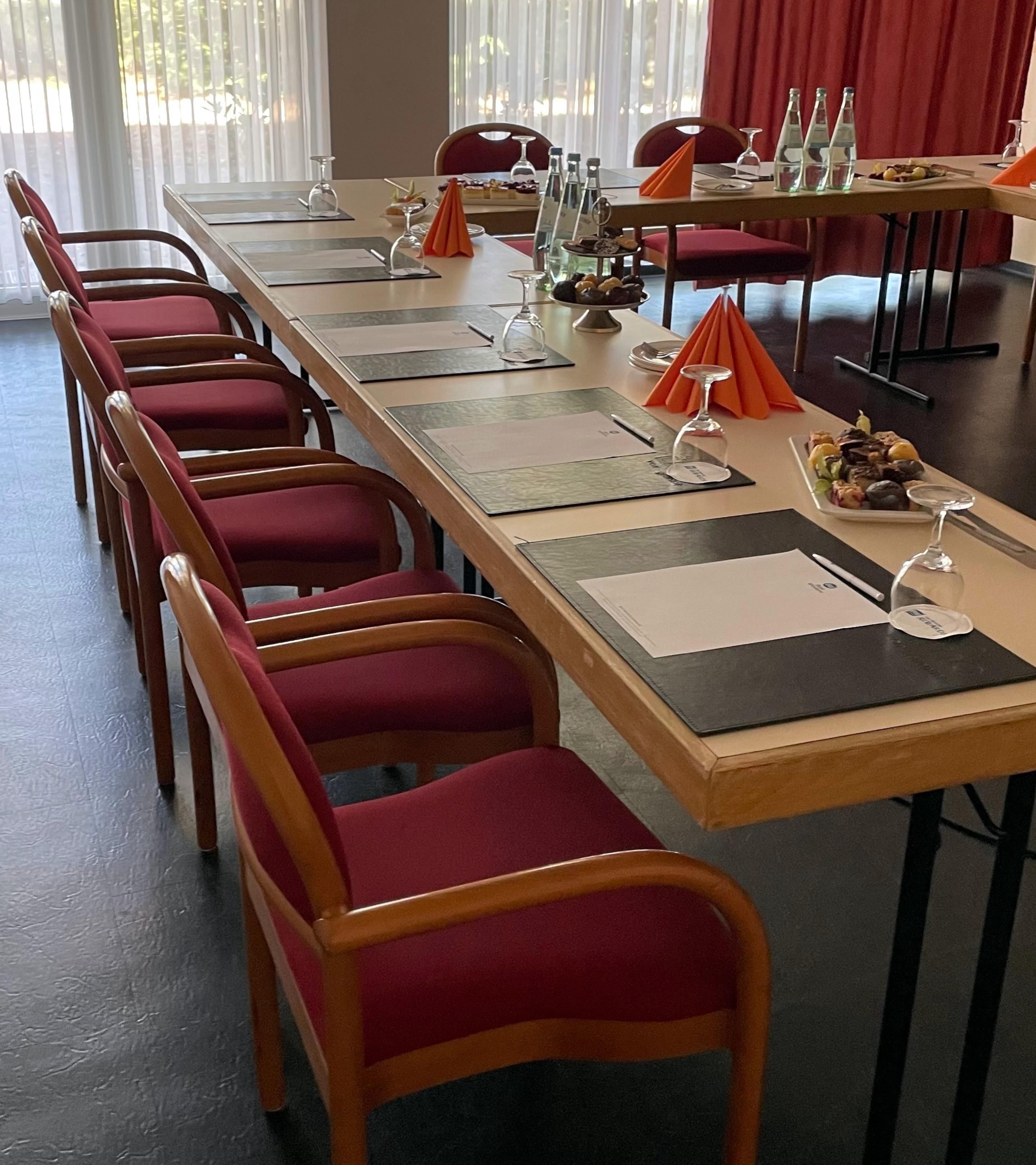 A conference room with a long table, multiple chairs, and various items like wine glasses, plates, and napkins.