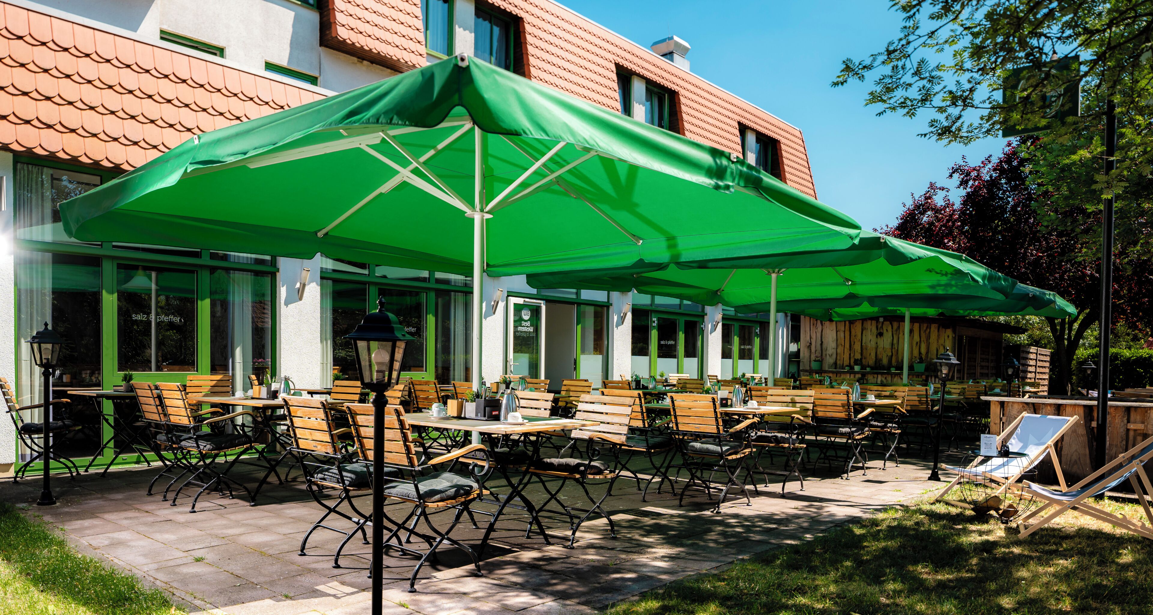 An outdoor seating area with tables and chairs, covered by a large green umbrella.
