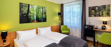 A hotel room with a large bed, two chairs, a desk with a computer, and two wall-mounted lamps.