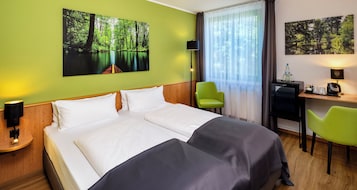 Habitación de hotel con una cama grande, dos sillones, un escritorio con una computadora y dos lámparas de pared.