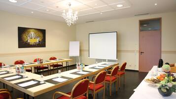 A conference room with a long table, red chairs, a projector screen, and a painting on the wall.