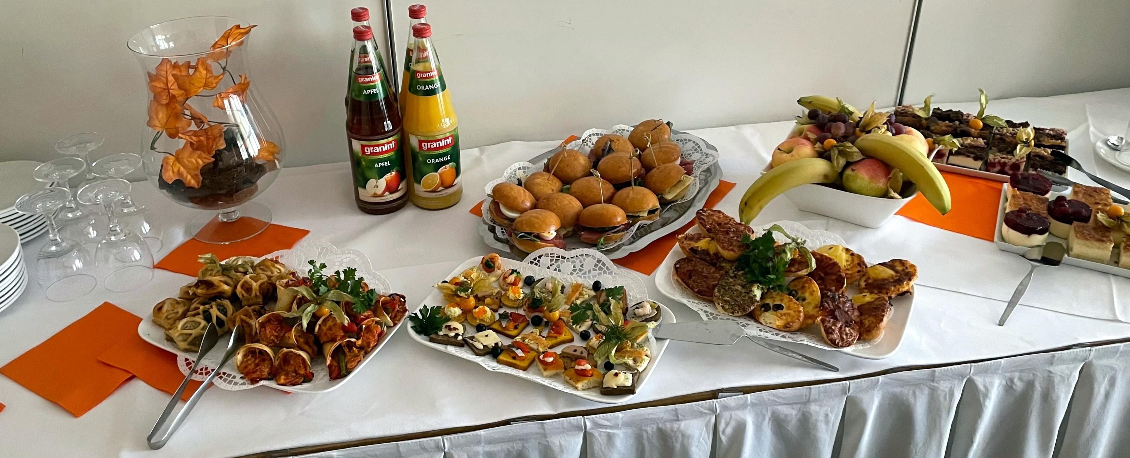 Une table garnie de divers aliments, notamment des sandwichs, des fruits et des amuse-gueules, ainsi que des bouteilles de boissons.