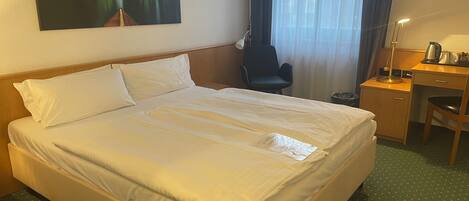 A hotel room with a large bed, a desk with a chair, a lamp, and a painting on the wall.