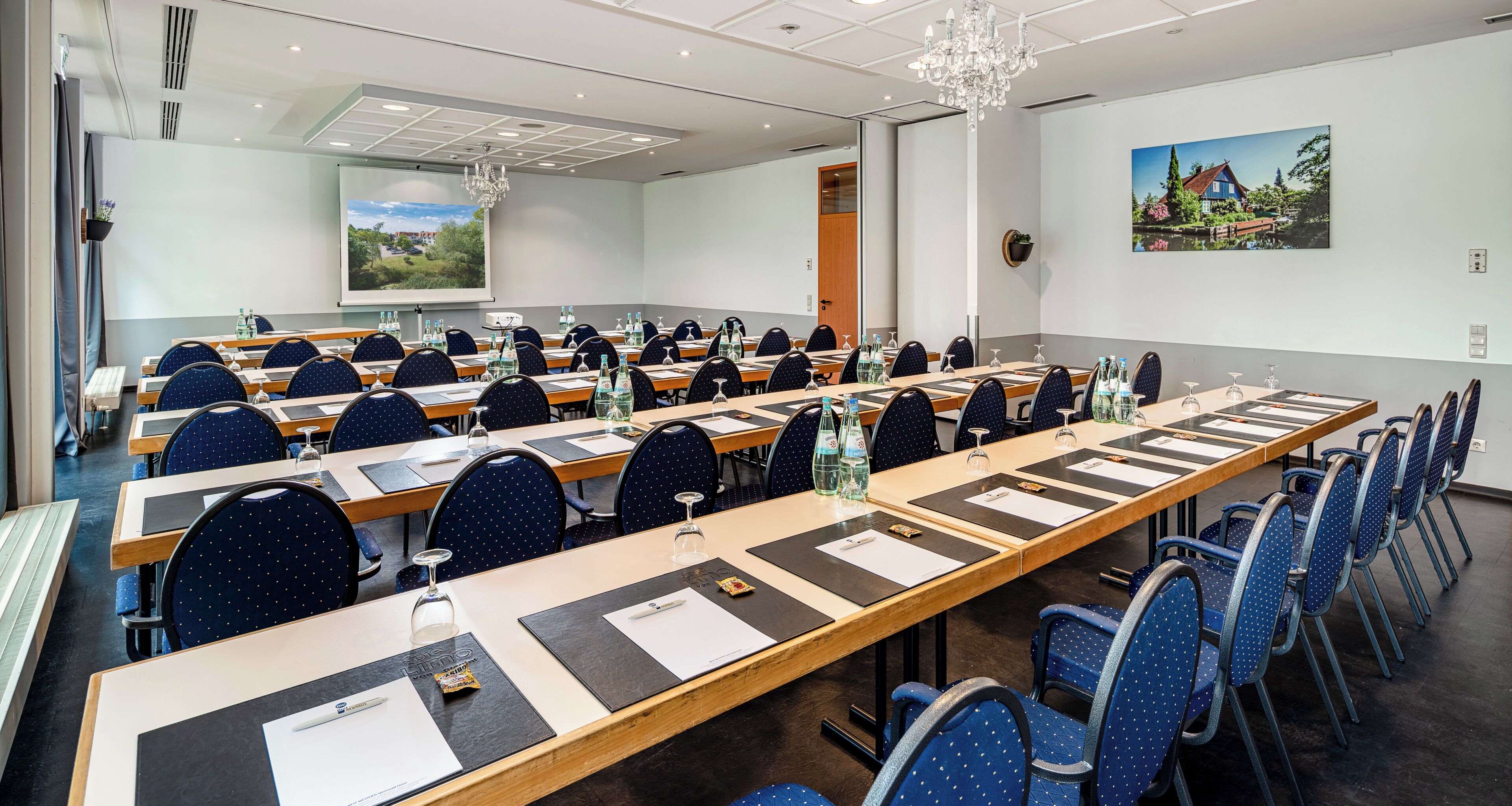 Un salón de conferencias con largas mesas, sillas y una pantalla de proyector.