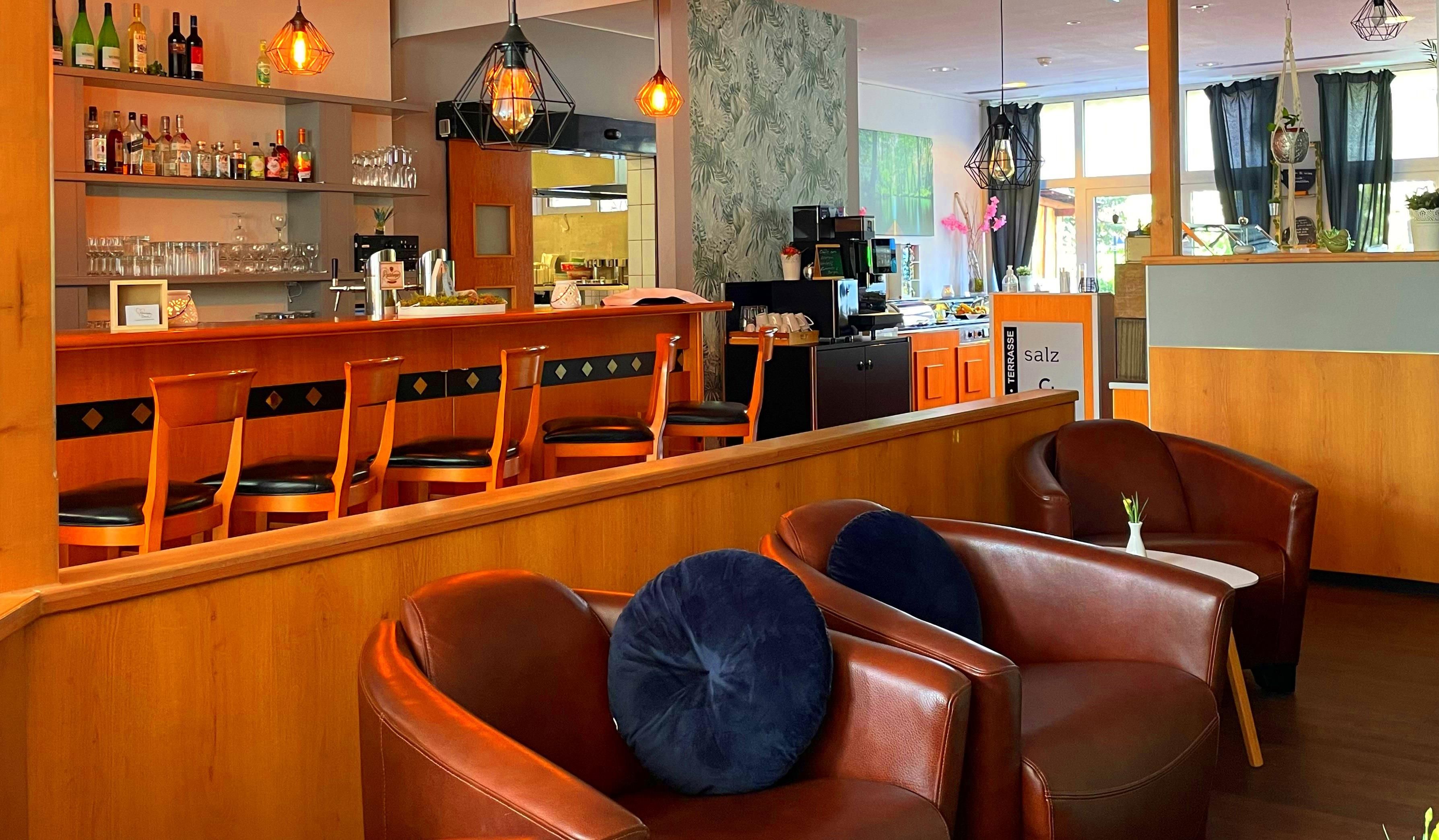 A bar area with wooden chairs and a counter, a seating area with leather chairs, and a view of the kitchen in the background.