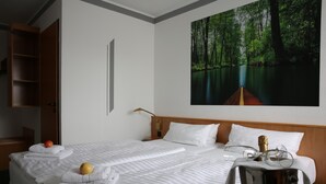 Habitación de hotel con una cama grande, una mesita de noche, un armario de madera, un cuadro de un bosque y una botella de champán.