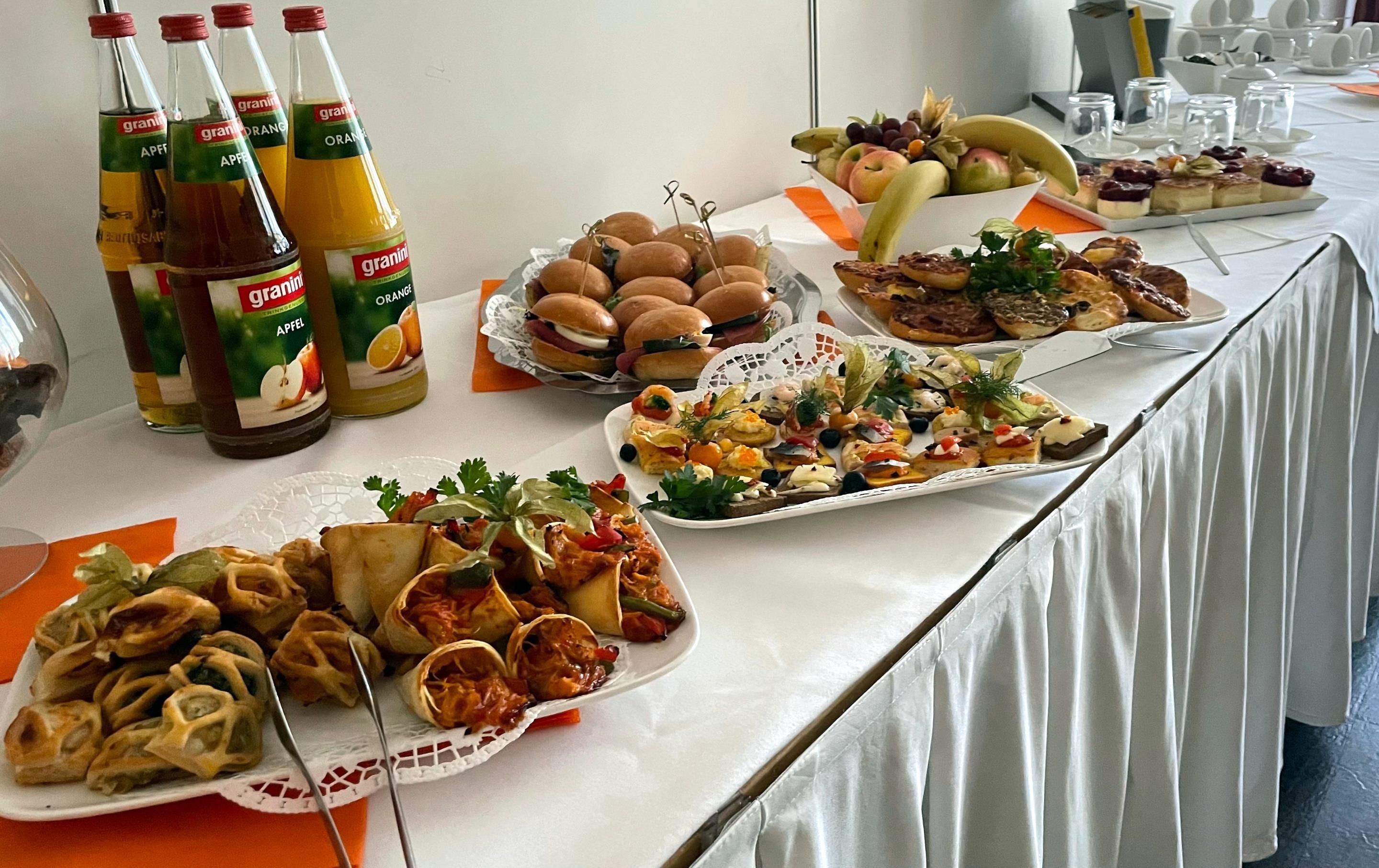 Una mesa de buffet con diversos alimentos, como sándwiches, pasteles y una variedad de jugos.