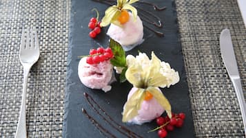 Un plato de postre con tres bolas de helado rosa, adornado con bayas rojas y hojas verdes, sobre un plato de pizarra oscura.