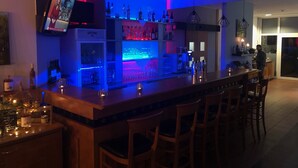 Un área de bar moderna con mostrador, asientos y una pantalla de televisión.