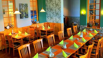 Un restaurant amb taules i cadires de fusta, parets verdes i una llar de pedra.