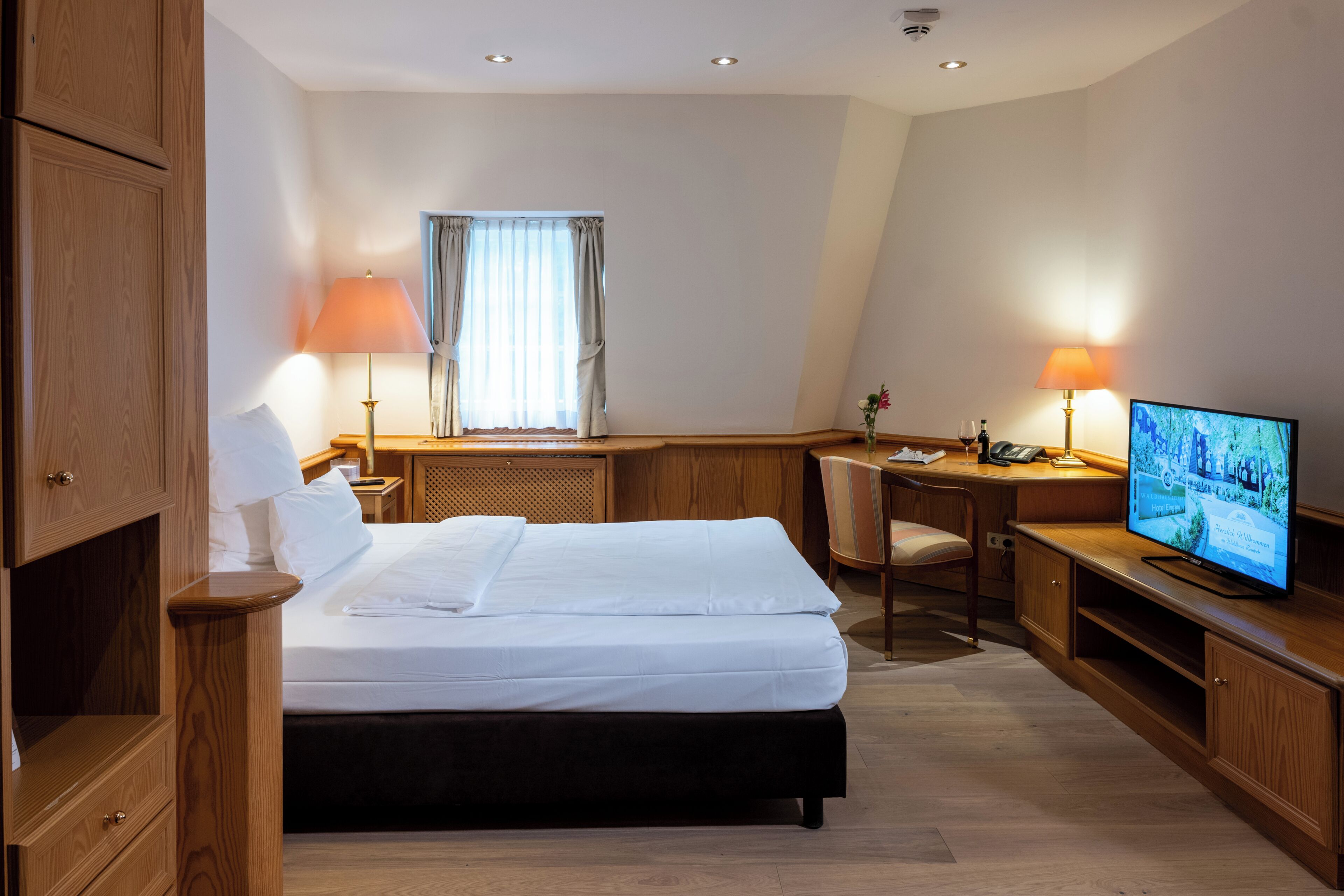 Ein Hotelzimmer mit Bett, Schreibtisch, Fernseher und einem Vorhangfenster.