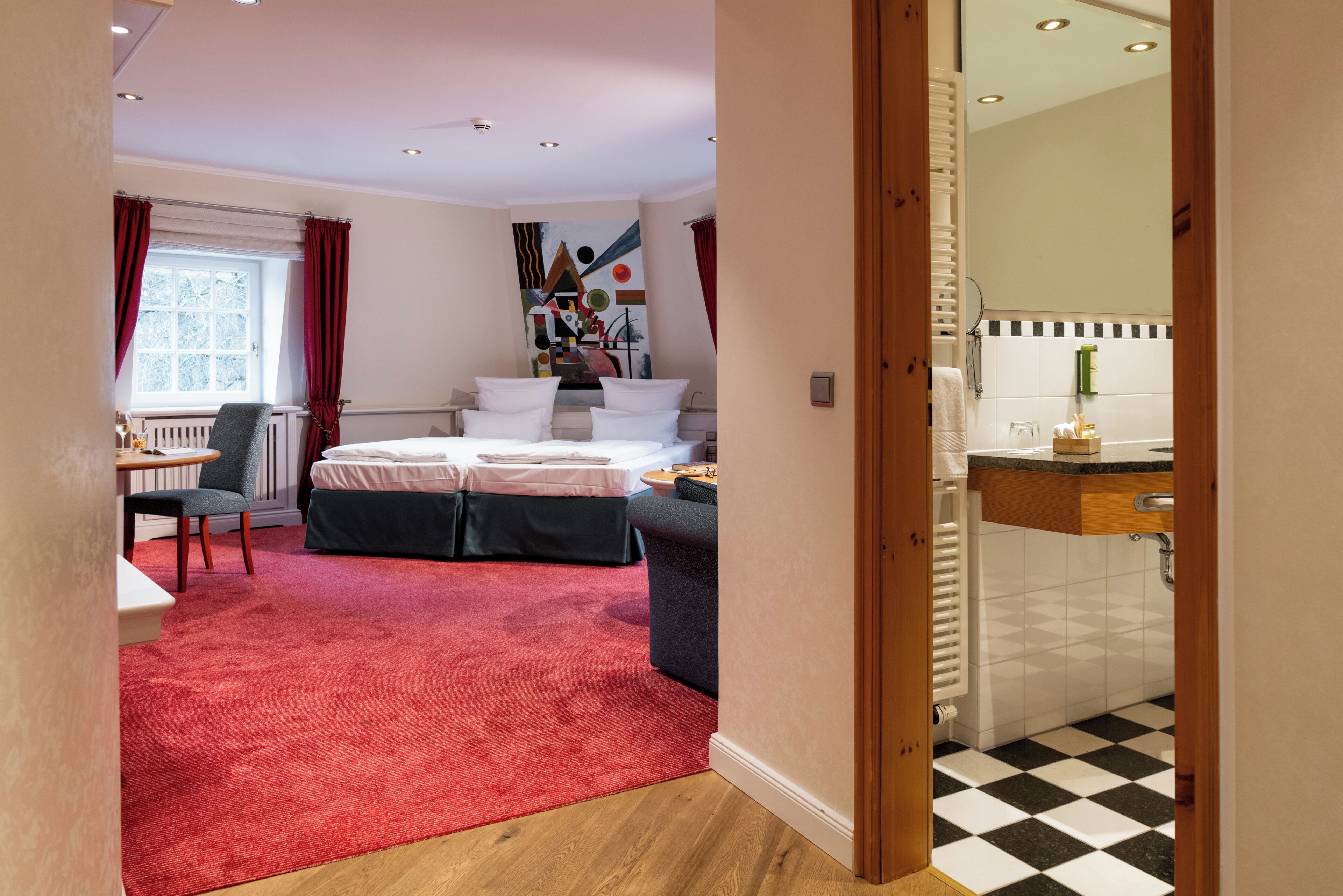 Une chambre d’hôtel avec un lit, un bureau, une chaise, une moquette rouge et une vue sur l’extérieur.