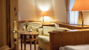 A hotel room with a bed, a round table with a vase of flowers, a sofa, a lamp, and a window with curtains.