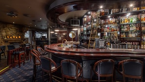 A bar area with a curved counter, multiple stools, and a variety of liquor bottles. - Waldhaus Reinbek (Reinbek)
