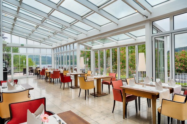 A spacious indoor dining area with high ceilings and large windows, featuring tables and chairs arranged for dining. - Welcome Hotel Meschede/Hennesee (Meschede)
