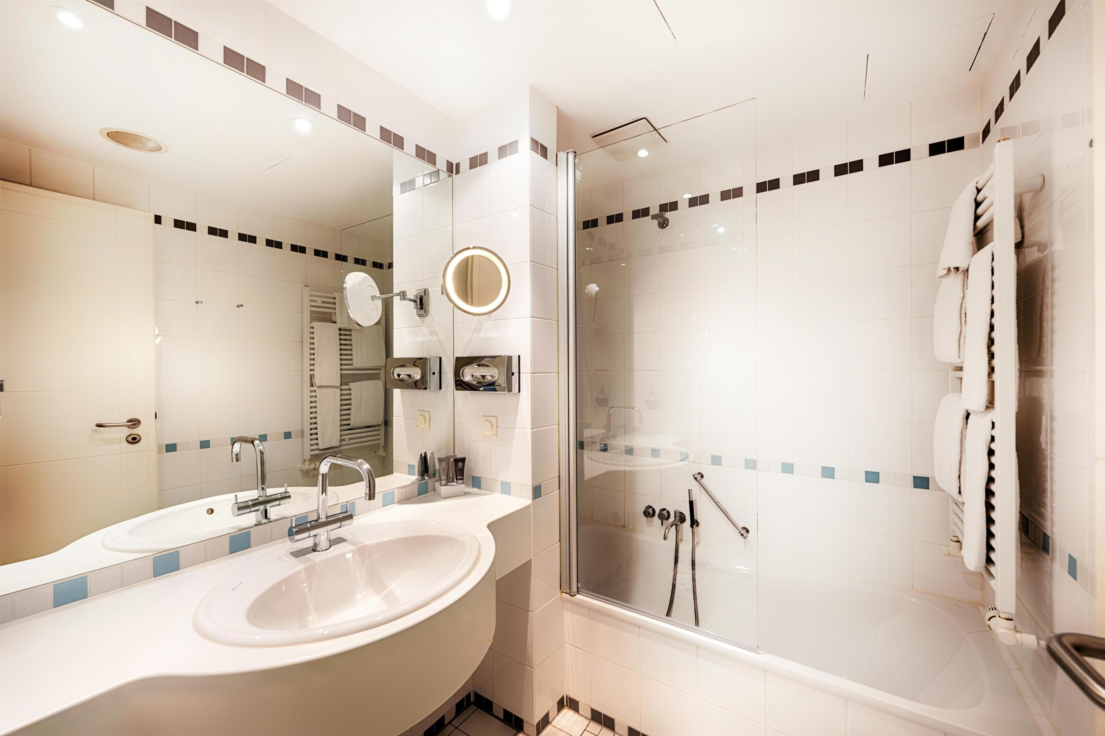 A modern bathroom with a large mirror, two sinks, a shower, and a towel rack.