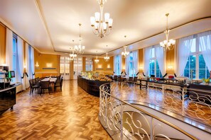 Un espacioso vestíbulo de hotel con piso de madera, una zona de bar central y múltiples candelabros.