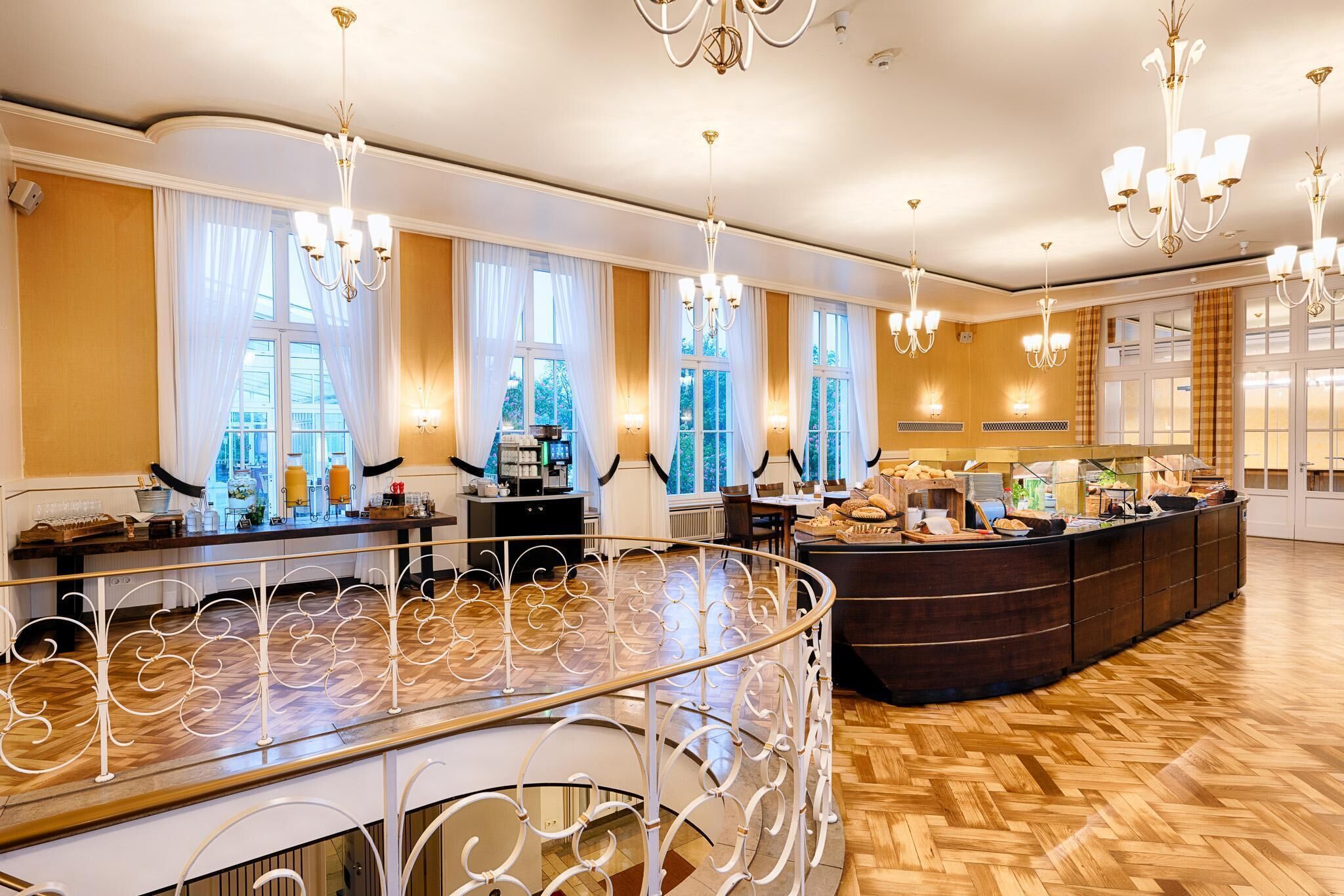 A spacious hotel lobby with a curved reception desk, chandeliers, and large windows with curtains.