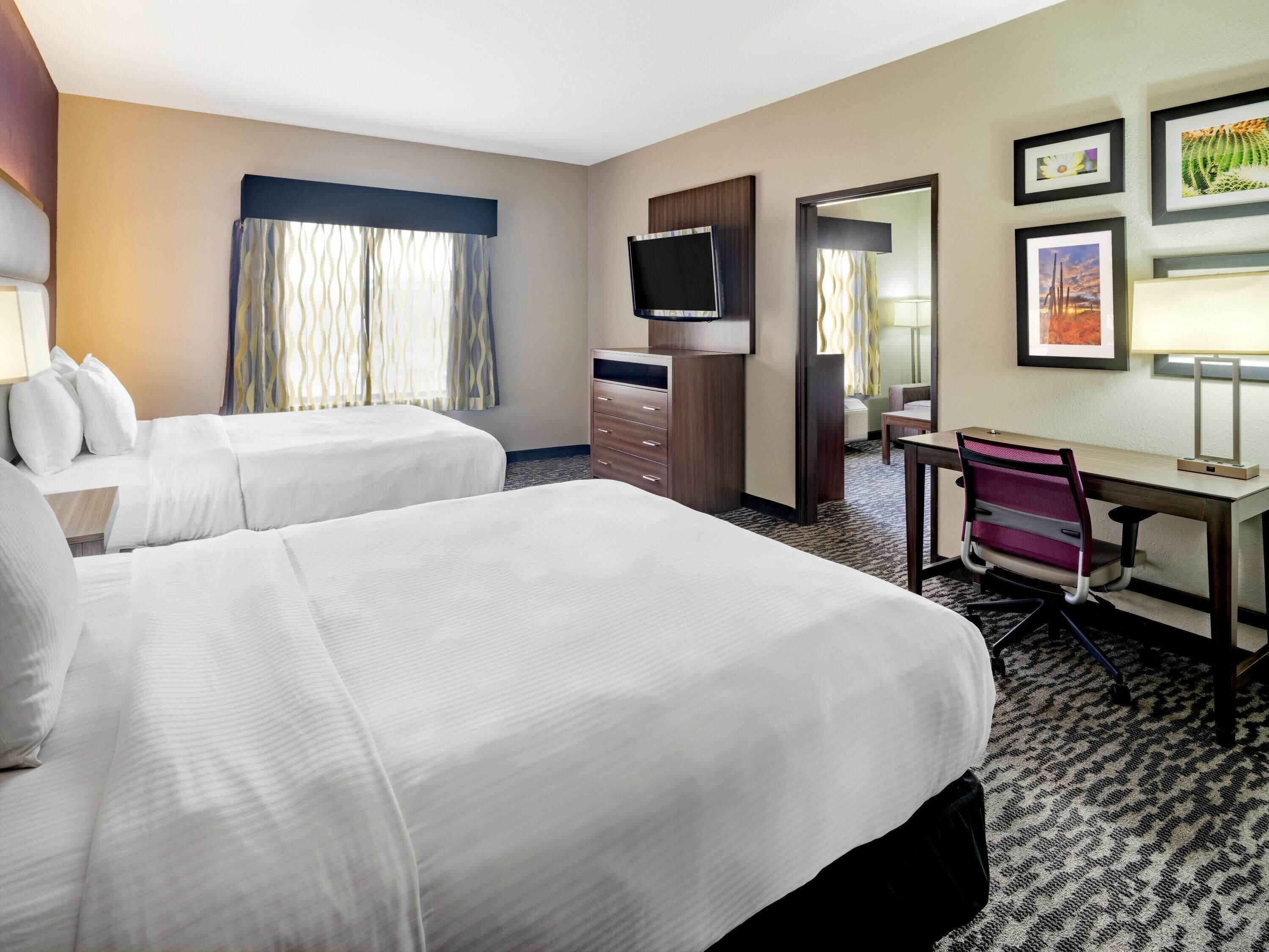 A hotel room with two beds, a desk, a chair, a TV, and framed pictures on the wall.