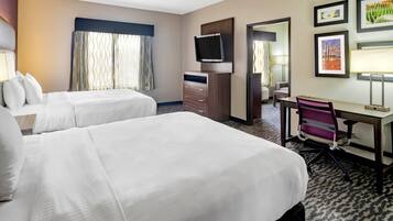 A hotel room with two beds, a desk, a chair, a TV, and framed pictures on the wall.