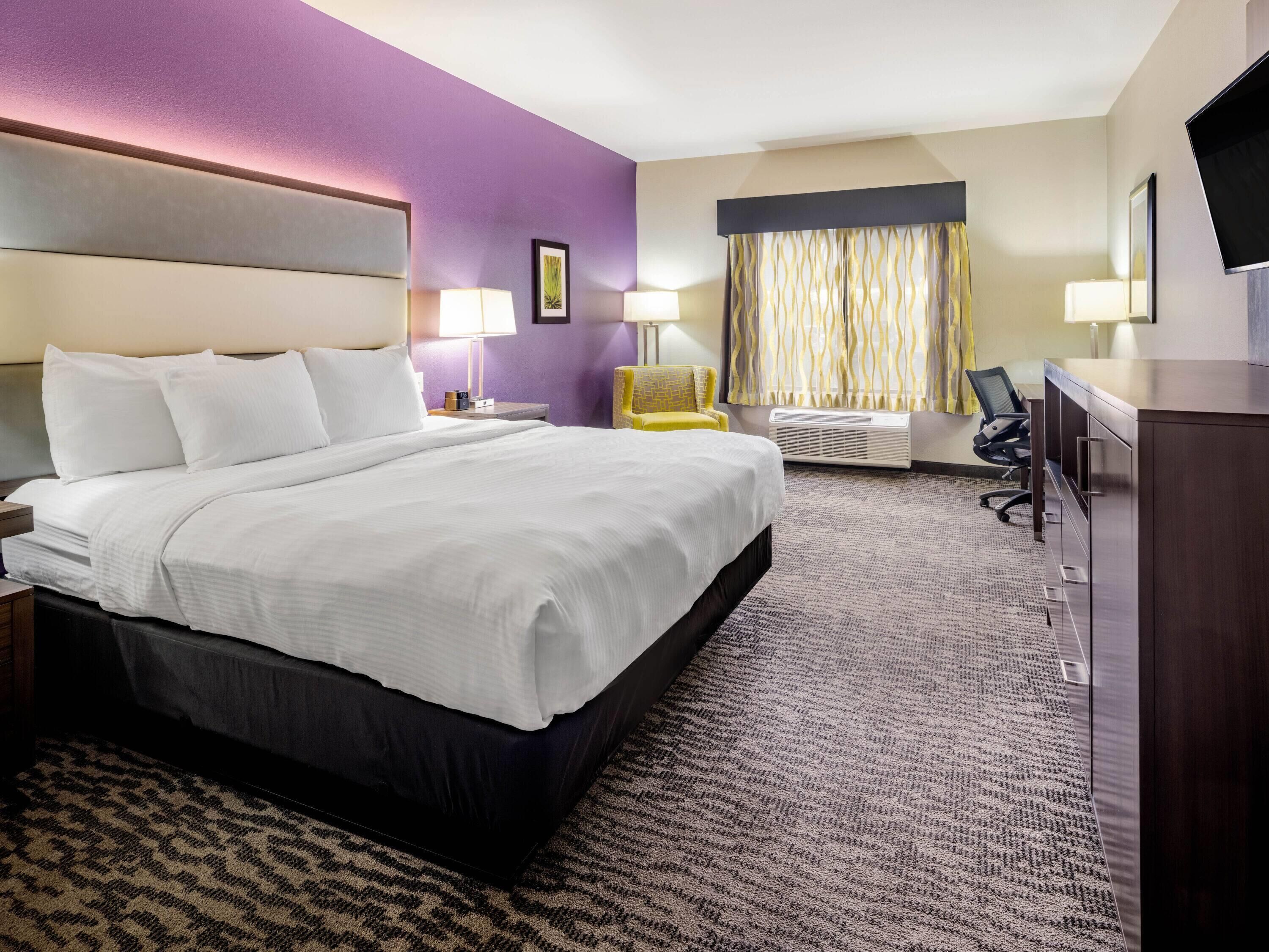 A hotel room with a large bed, a desk, a chair, a TV, and a window with curtains.