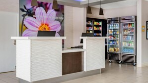 A modern reception area with a white reception desk, pendant lighting, a digital display with a floral image, and a refrigerated beverage display.