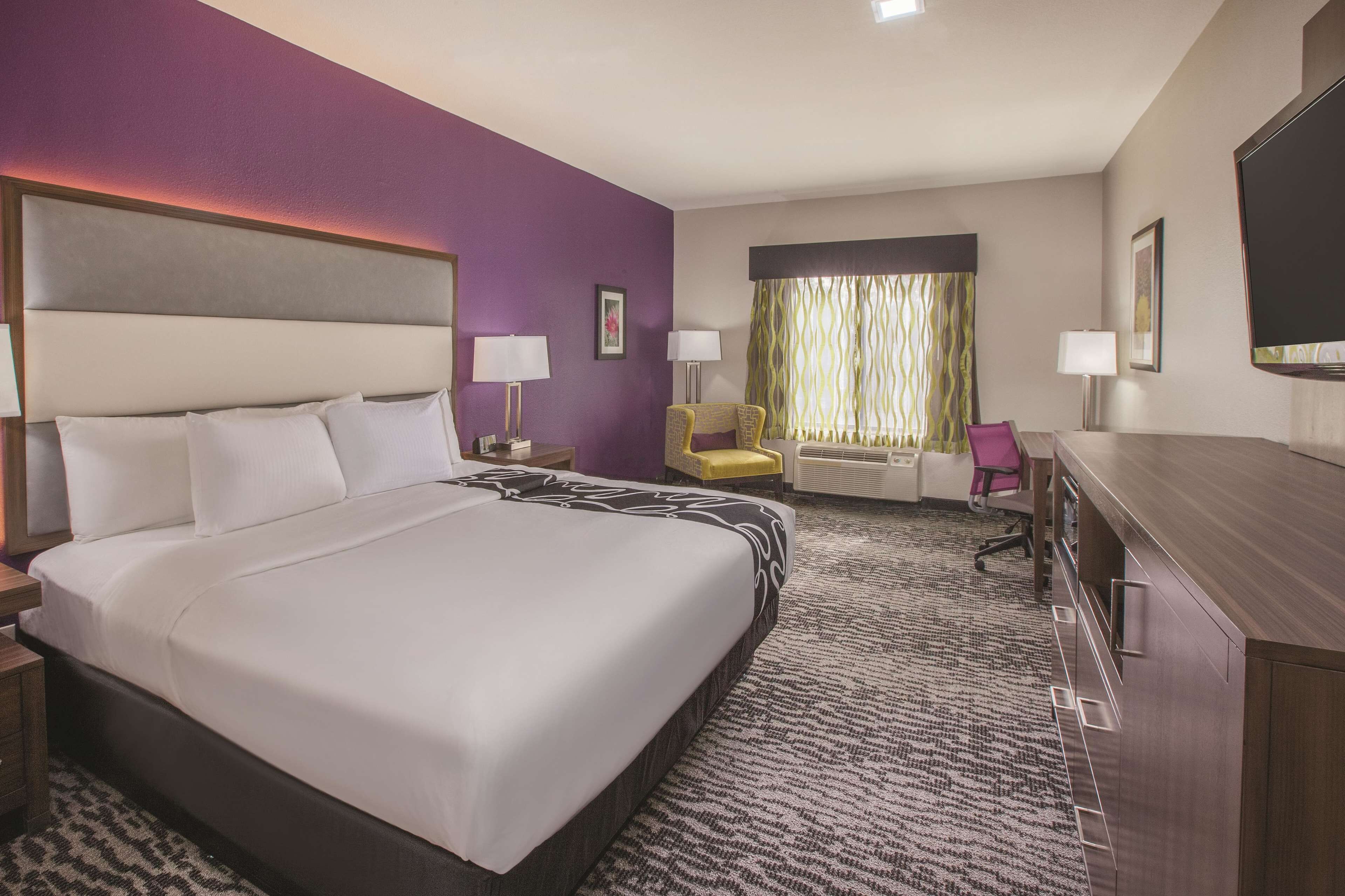 A hotel room with a large bed, a desk, a chair, and a television.