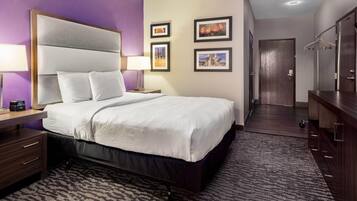 A hotel room with a large bed, a nightstand, a dresser, and a walk-in closet.