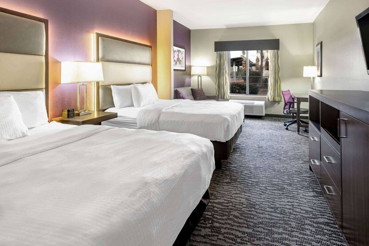 Une chambre d’hôtel avec deux lits, un bureau, une chaise et une grande fenêtre avec des rideaux.
