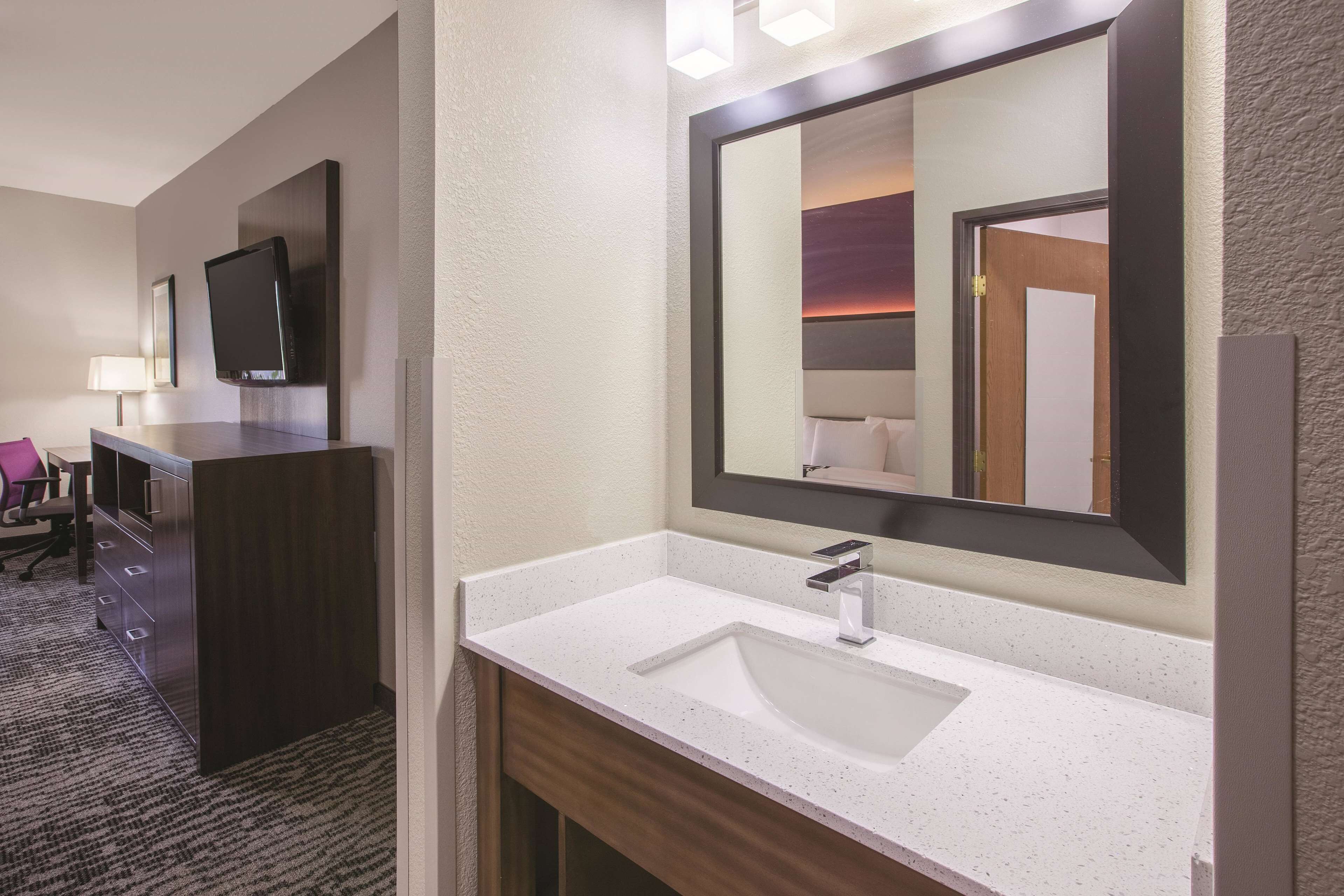 A modern bathroom with a large mirror, a white sink, and a dark wooden vanity.