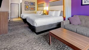 A hotel room with two beds, a sofa, a coffee table, and a desk.