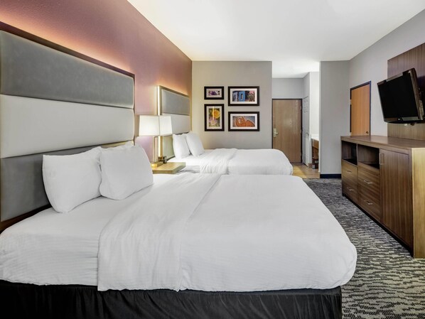 Una habitación de hotel con dos camas, un escritorio, un televisor y obras de arte en la pared.