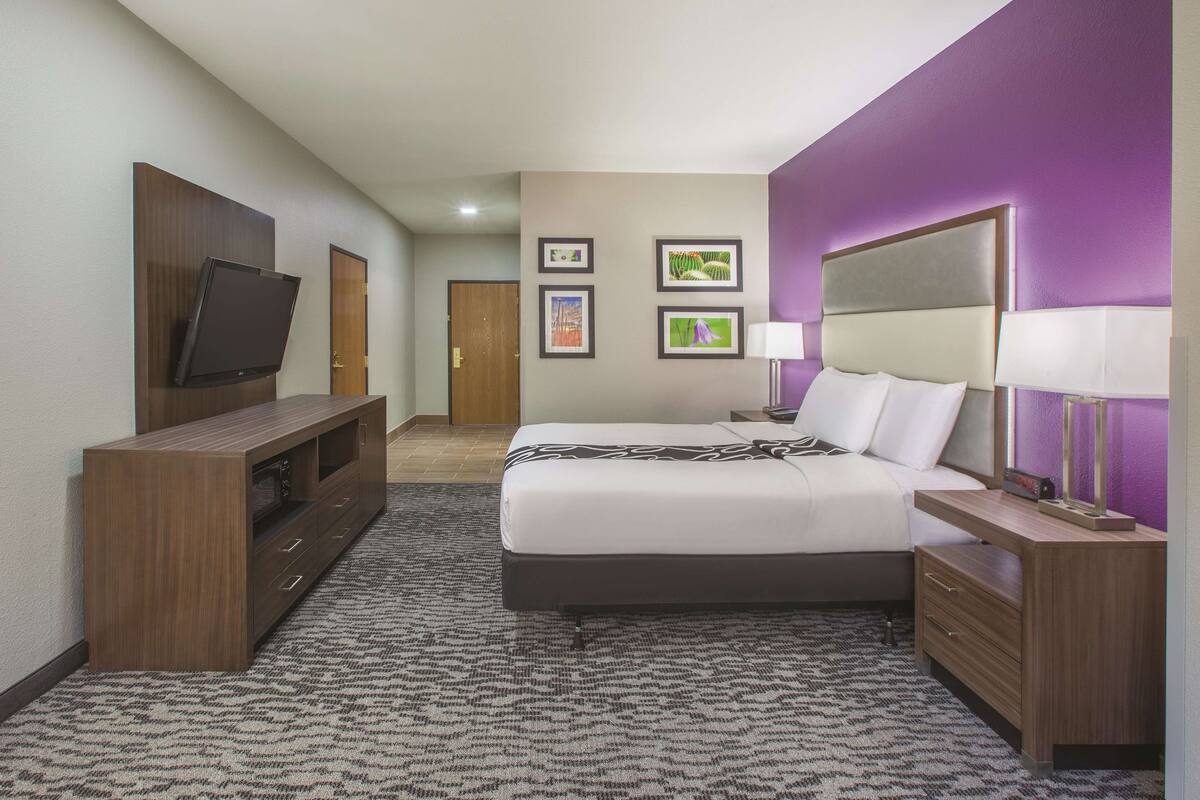Une chambre d’hôtel avec un lit, un téléviseur posé sur un meuble, un bureau avec une lampe et des tableaux encadrés accrochés au mur.