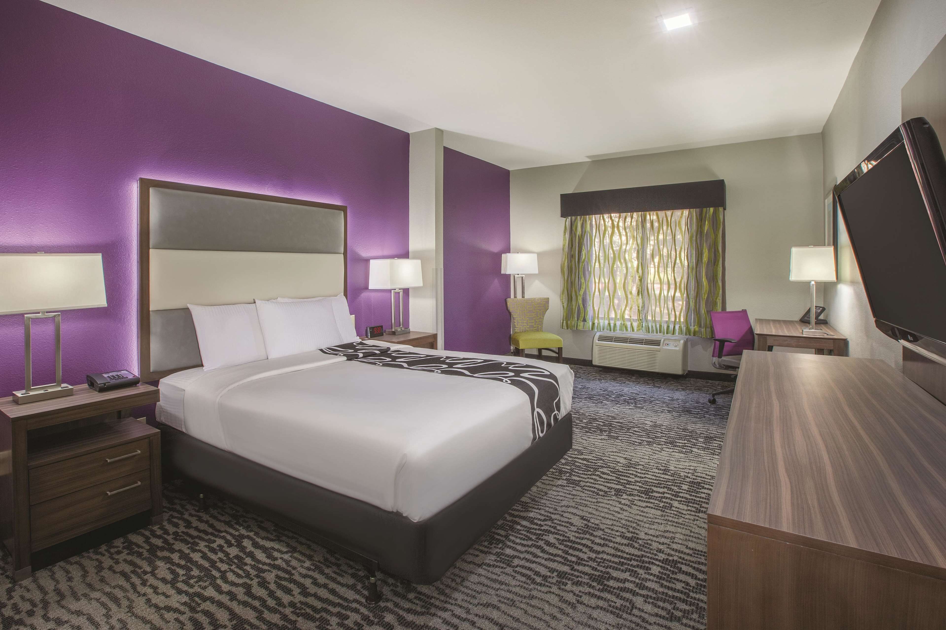 Une chambre d’hôtel avec un grand lit, des tables de chevet avec des lampes, un bureau avec une chaise, une télévision et une fenêtre avec des rideaux.