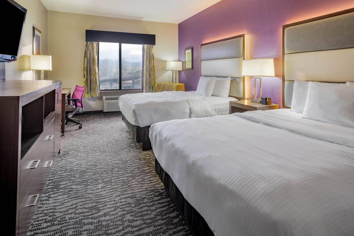 Une chambre d’hôtel avec deux lits, un bureau, une chaise et un téléviseur.