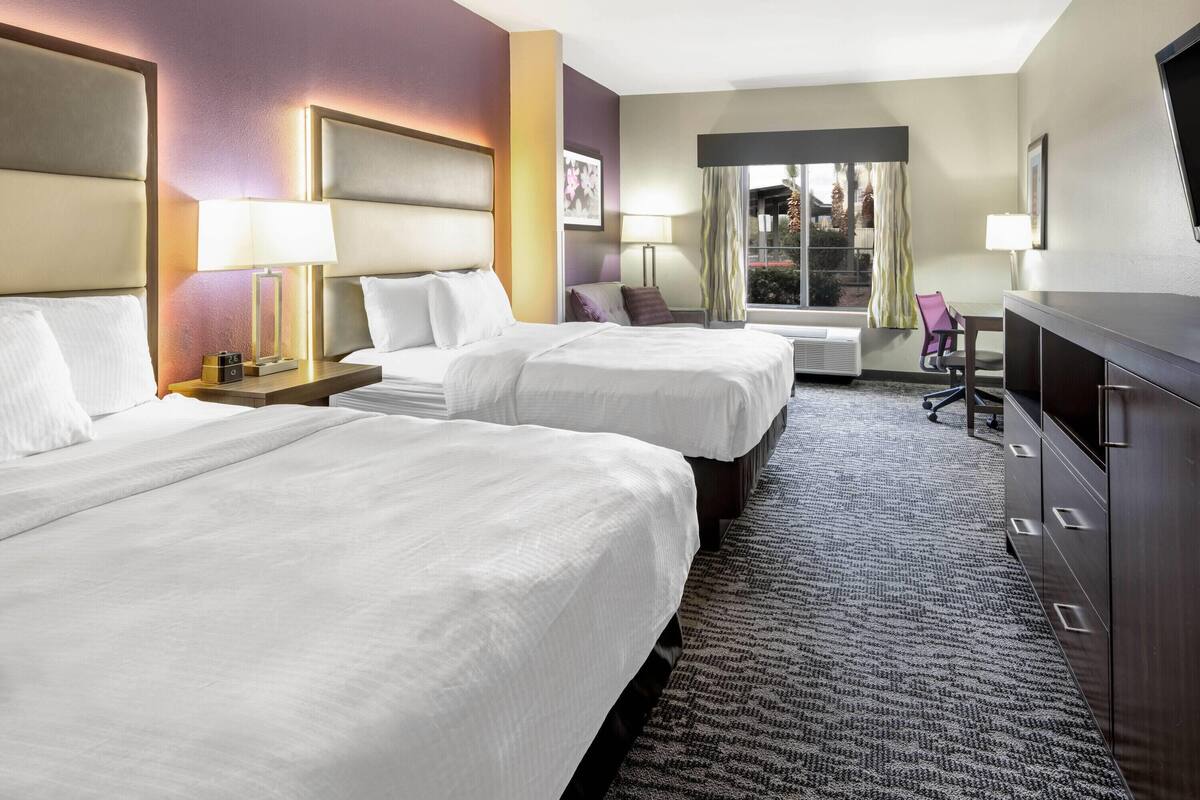 Une chambre d’hôtel avec deux lits, un bureau, une chaise et une commode.