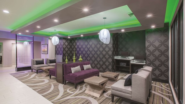 A modern lobby with a purple sofa, grey armchairs, and a patterned carpet.