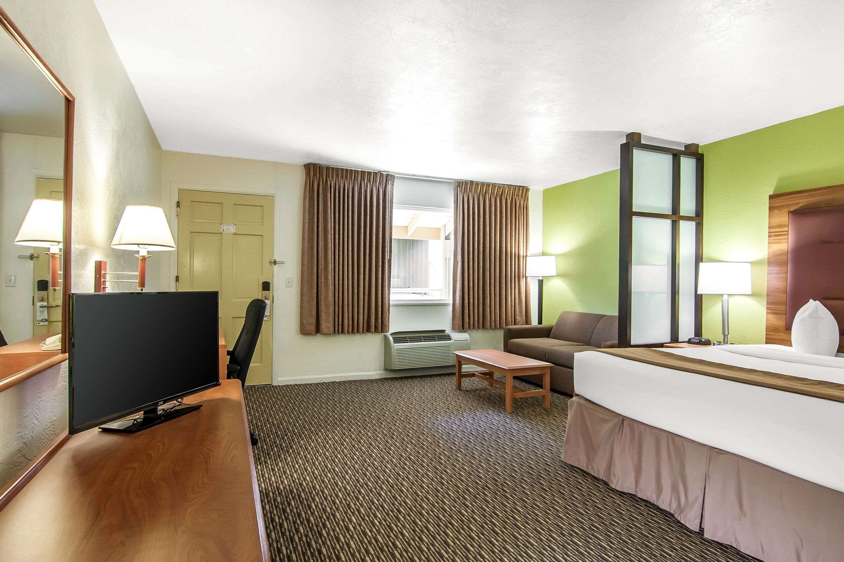 A hotel room with a bed, desk, TV, and a view of the outdoors.