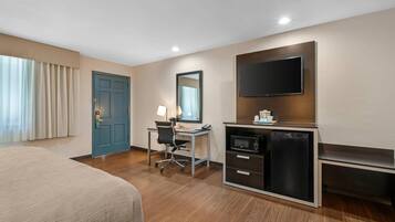 A hotel room with a bed, desk, chair, TV, microwave, and a small refrigerator.