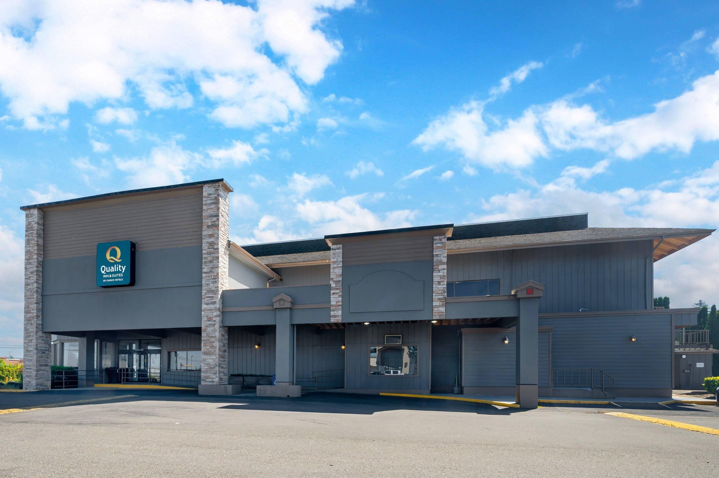 A hotel with a large garage entrance, a sign with 'Quality' and 'Hotel & Suites,' and a clear sky.