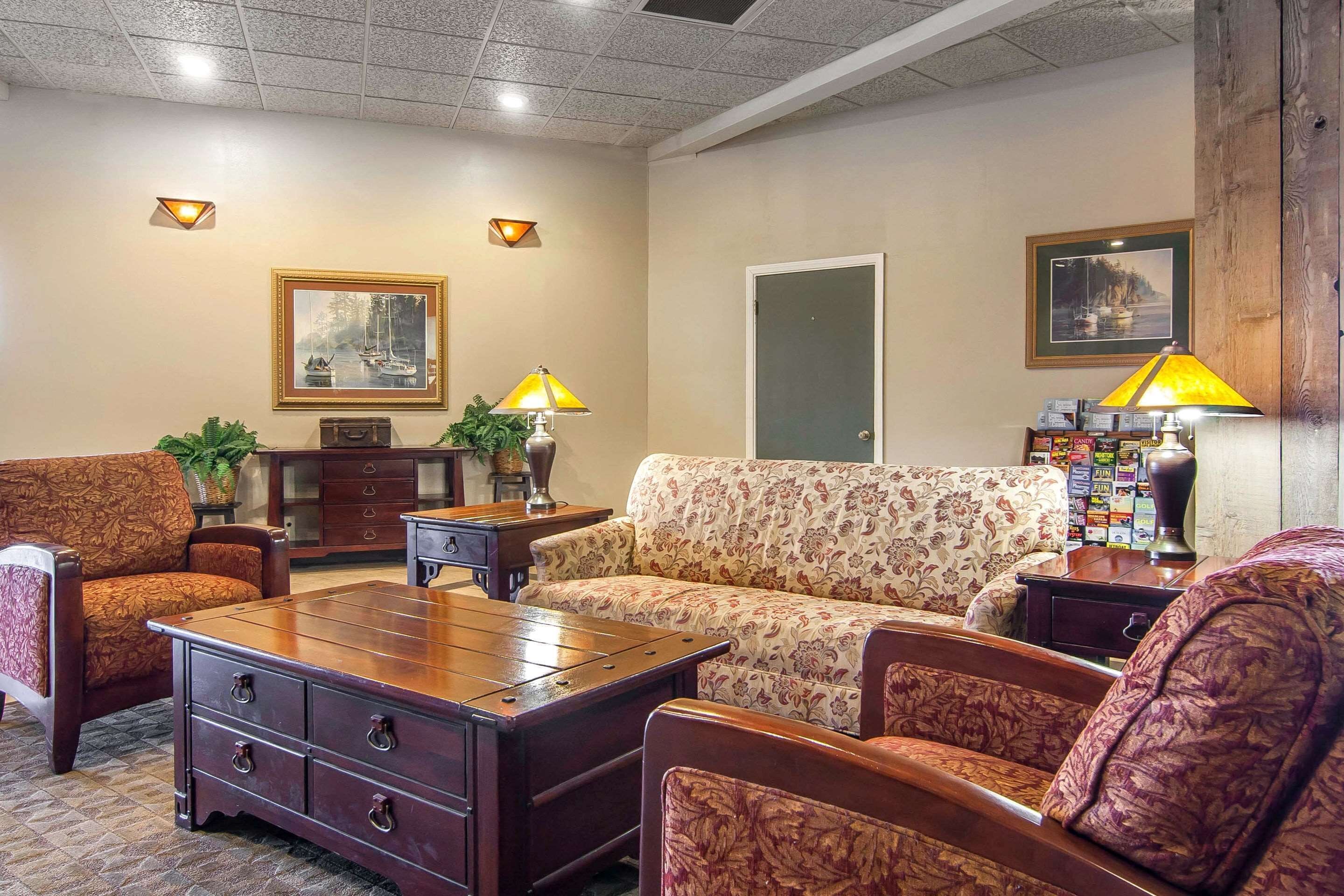 A well-lit living room with a sofa, armchairs, a wooden coffee table, and two lamps. There are framed pictures on the walls and a door in the background.