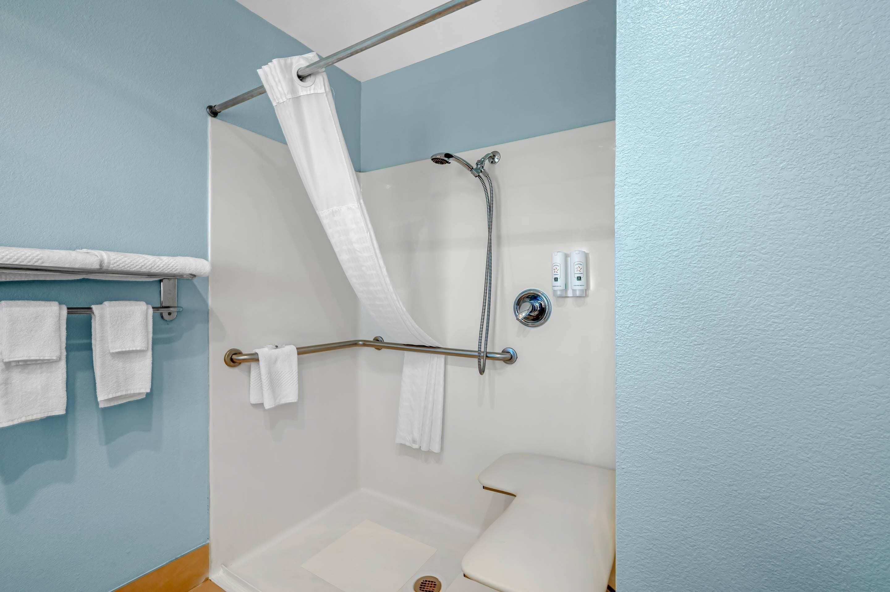 A shower with a grab bar, a white toilet, and a towel rack with towels.