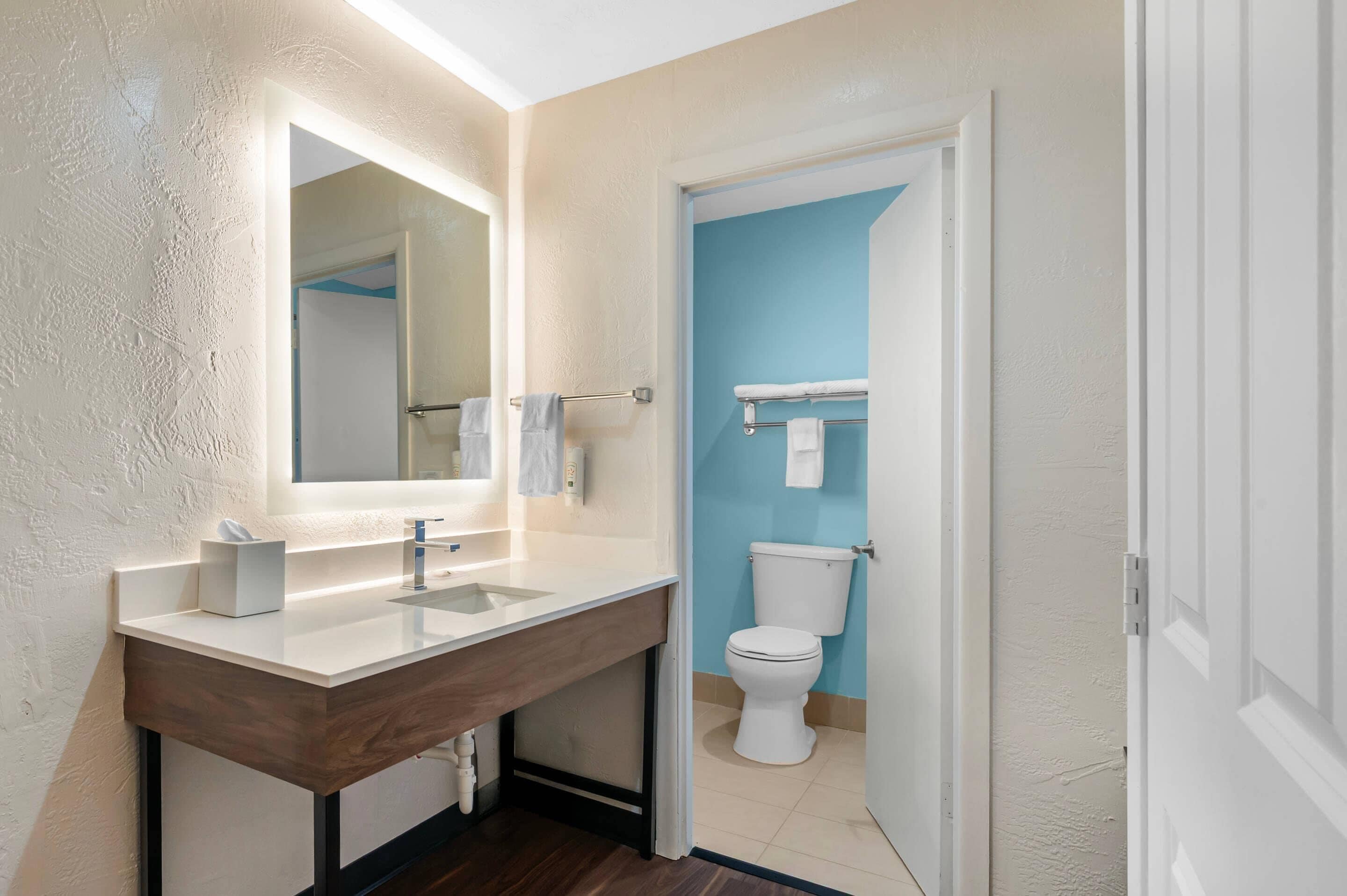 A bathroom with a wooden vanity, a large mirror, a toilet, and a towel rack.