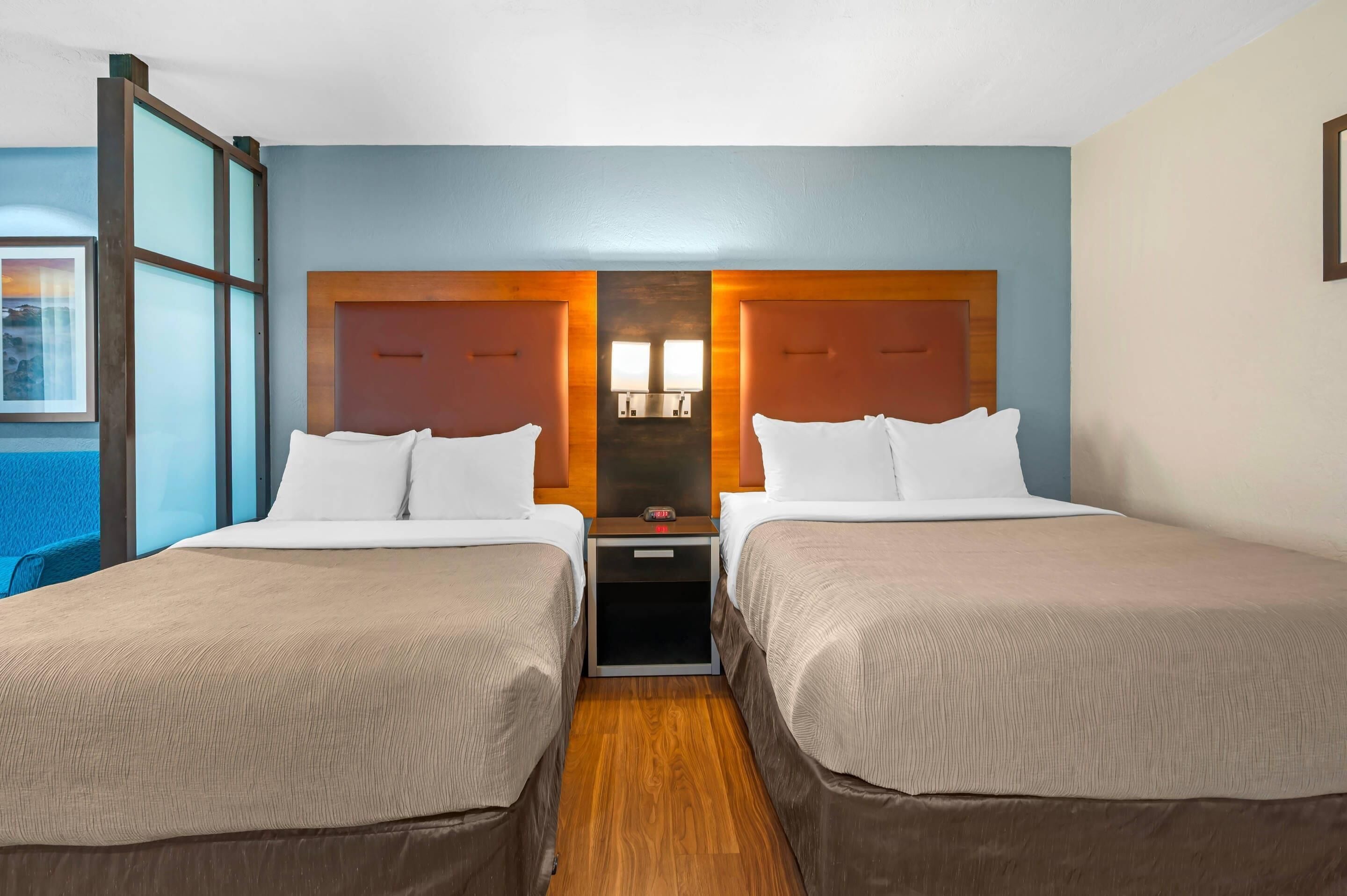 A hotel room with two beds, a nightstand, a wooden headboard, and a window with a view.