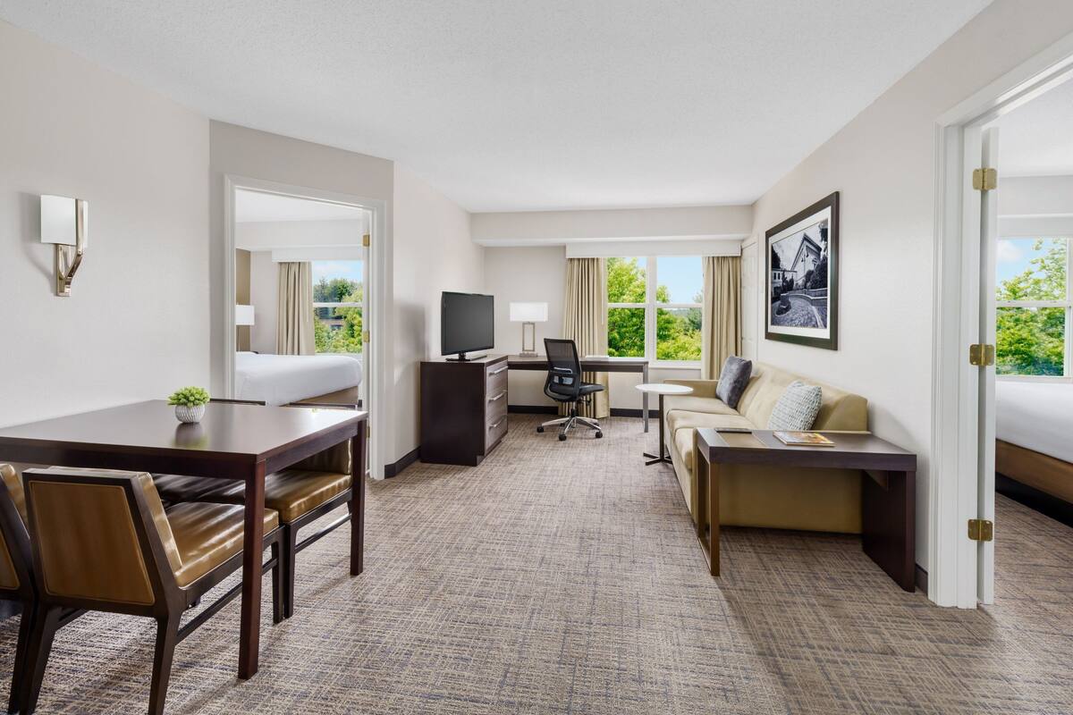 Ein Hotelzimmer mit Esstisch, zwei Sofas, einem Schreibtisch mit Computer und einem Fernseher.