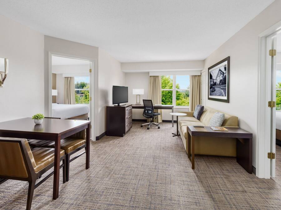 A hotel room with a dining table, two sofas, a desk with a computer, and a TV.